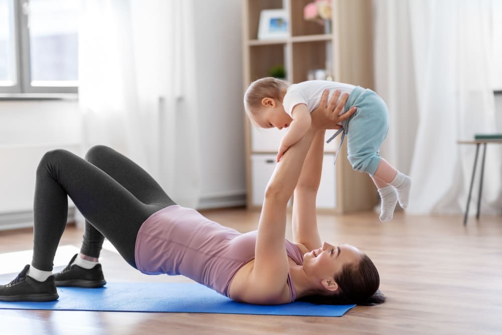 Happy smiling mother with little baby exercising pelvic lifts at home